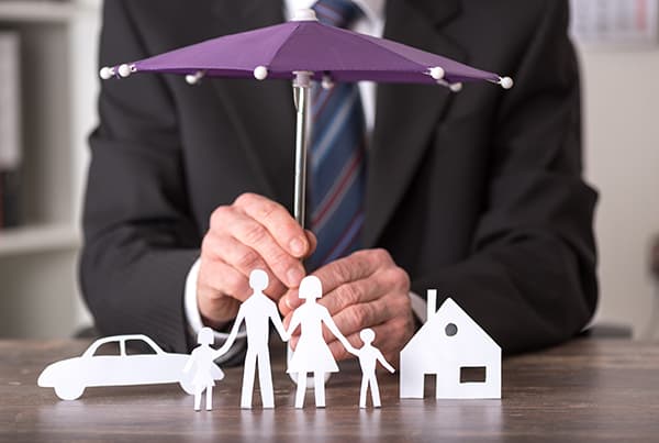 insurance agent in suit holding umbrella over paper cutout family and house umbrella insurance